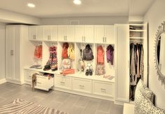 a white closet filled with lots of coats and purses next to a mirror on the wall