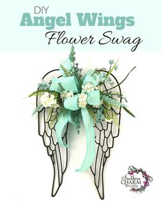 an angel wings decoration with flowers and green ribbon on it's back side, against a white background