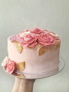 a hand holding a cake with pink frosting and flowers