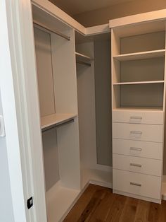 an empty walk in closet with white drawers and shelves on each side, next to a wooden floor