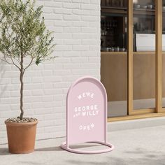 a pink sign that says we're george and willy open next to a potted tree