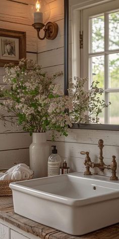 a white sink sitting under a bathroom mirror next to a vase with flowers in it