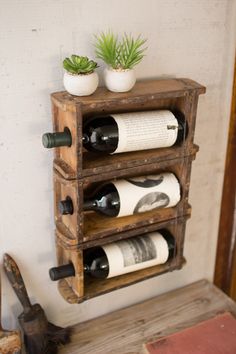 a wooden shelf with three wine bottles and two planters on top, sitting next to a wall