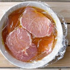 two pieces of meat wrapped in plastic sitting on top of a white bowl filled with orange liquid