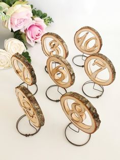 six wooden rings with numbers on them sitting next to flowers and a vase filled with pink roses