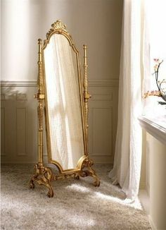 an ornate gold framed mirror sitting in front of a window next to a white curtain