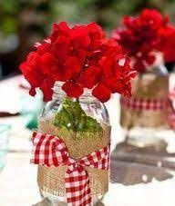 red flowers are in mason jars with burlocks and bows on the tablecloth