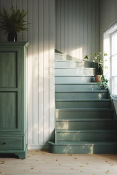 a green cabinet sitting next to a set of stairs with plants on the top and bottom