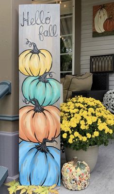 a painted sign with pumpkins on it sitting in front of a flower pot and yellow flowers