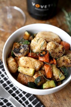 a white bowl filled with chicken and veggies on top of a wooden table