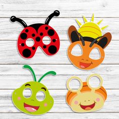 three masks with different designs on them sitting on a wooden surface, one is wearing a ladybug mask and the other has an antelope