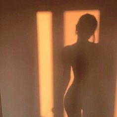 a nude woman standing in front of a window with the sun shining on her body