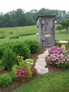 a small wooden outhouse sitting in the middle of a flower filled garden with pink and yellow flowers