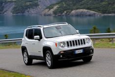 a white jeep driving down a road next to a lake