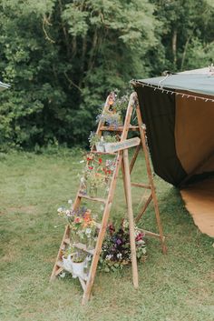 a wooden ladder with flower pots on it sitting in the grass next to a tent