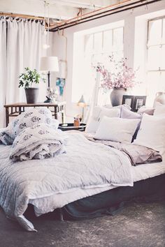 an unmade bed with pillows and blankets on it in front of a large window