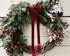 a christmas wreath hanging on the side of a building with red ribbon and pine cones