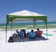 two people sitting under a tent on the beach next to some chairs and coolers