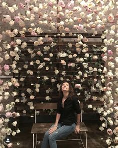 a woman sitting on a bench in front of a flower wall