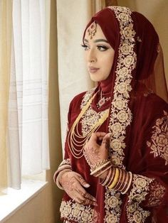 a woman in a red and gold wedding outfit standing next to a window with her hands on her hips