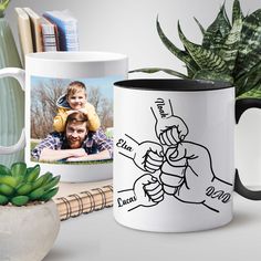 two coffee mugs sitting on top of a table next to a potted plant