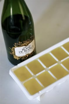 an ice cube next to a bottle of wine on a white counter top with a brown label