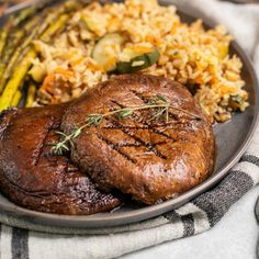 a plate full of meat, rice and asparagus on a table with utensils