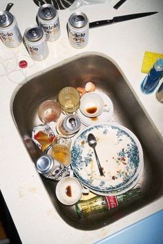 dirty dishes are sitting in the sink with empty cans on the counter top next to it