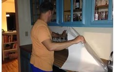 a man standing in front of a white paper on top of a kitchen counter next to blue cabinets