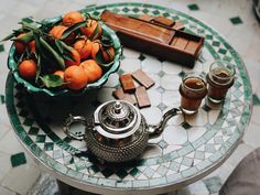 a bowl of oranges sitting on top of a table next to a tea pot