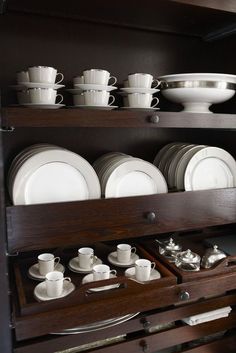 a wooden cabinet filled with white dishes and silverware