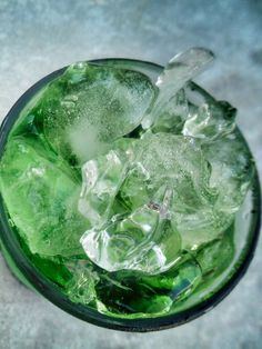 a glass filled with ice sitting on top of a cement floor next to a bottle