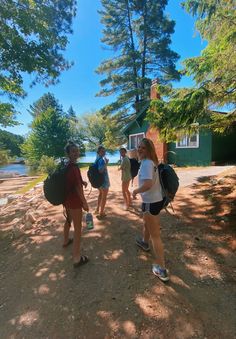 several people are walking on the dirt near some trees and water, with one person carrying a backpack