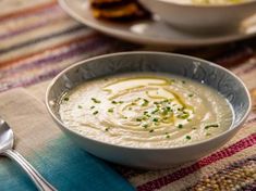 there is a bowl of soup on the table with two plates and spoons next to it