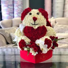 a teddy bear sitting in a red box with white and red flowers on the table