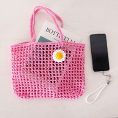 a pink crocheted bag with a flower on it next to a cell phone