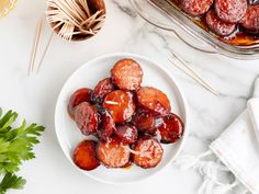 a white plate topped with sliced plums next to a glass dish filled with fruit