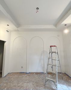 a ladder is standing in the middle of a room with white walls and arches painted on it