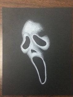 a chalk drawing of a scream mask on a blackboard with white paint and the mouth open