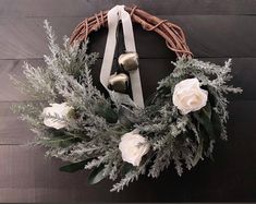 a wreath with white flowers and greenery hanging on a wooden wall next to two bells