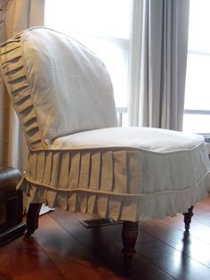 a white chair sitting in front of a window next to a lamp and wooden floor