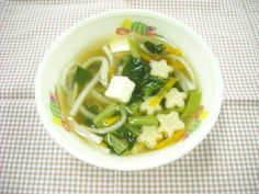 a white bowl filled with soup and vegetables on top of a checkered table cloth