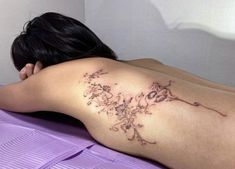 a woman laying on top of a bed with her back turned to the camera and tattoos on her arm