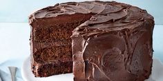 a chocolate cake on a white plate with one slice cut out and ready to be eaten