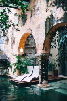 an outdoor swimming pool with lounge chairs and potted plants next to it, surrounded by stone archways