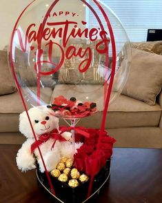 a teddy bear sitting in a basket filled with chocolates and roses next to a happy valentine's day sign