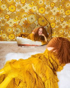 a woman in a yellow dress laying on the floor next to a flowered wall