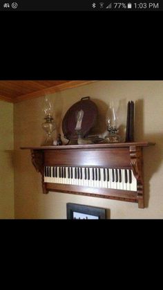 an old fashioned piano with wine glasses on it's shelf next to a clock