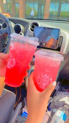 two people holding up drinks in their hands while sitting in the drivers seat of a car