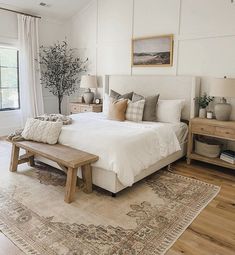 a bedroom with white walls and wood floors has a large rug on the floor next to the bed